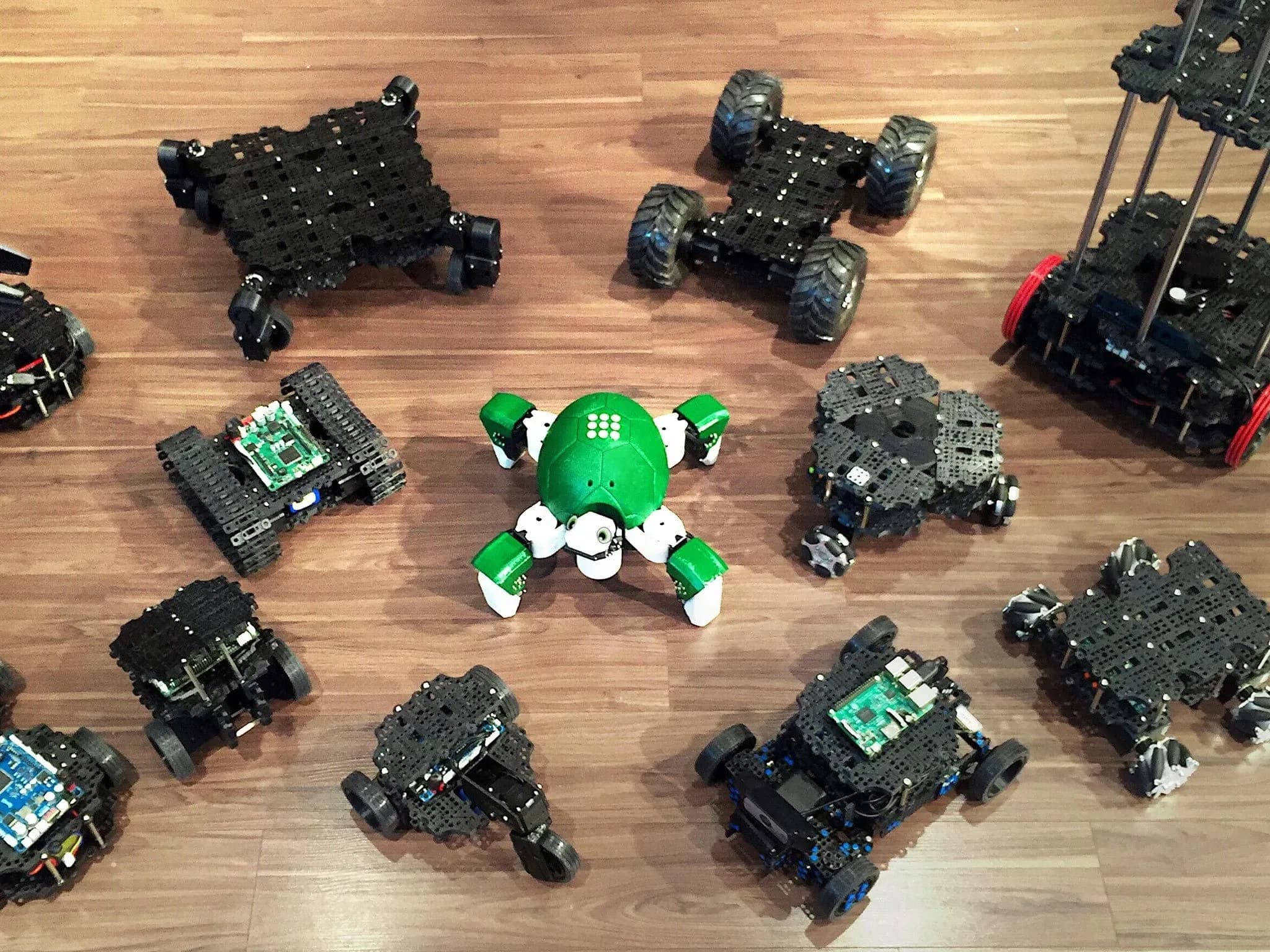 Дюжина вариантов TurtleBot 3 разных форм и размеров на деревянном полу.