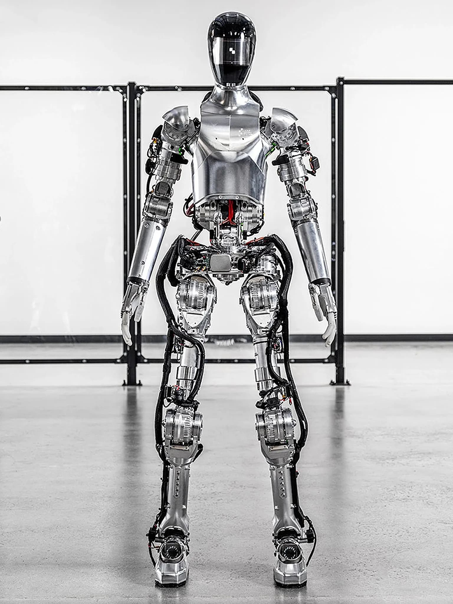 Робот Figure 01 — блестящий серебристый двуногий гуманоид с руками и шлемообразной головой — стоит на складе.