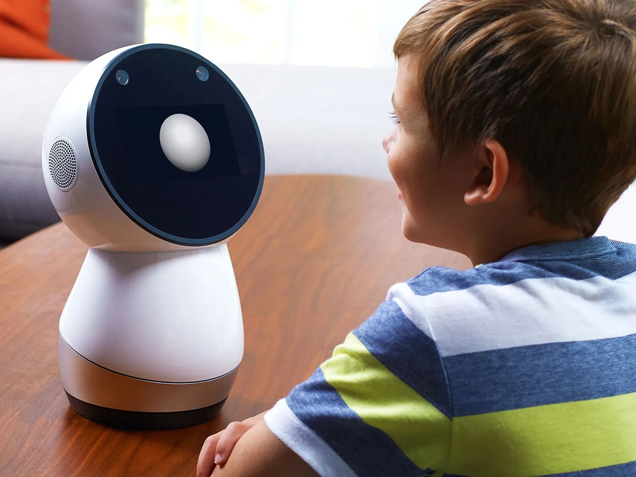Jibo — простой робот с круглым чёрным дисплеем и белым корпусом в форме кегли — стоит на столе и общается с маленьким мальчиком.