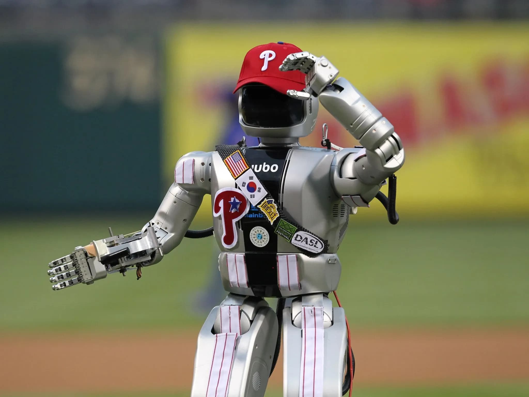 Робот стоит на бейсбольном поле в кепке Phillies и частях формы.