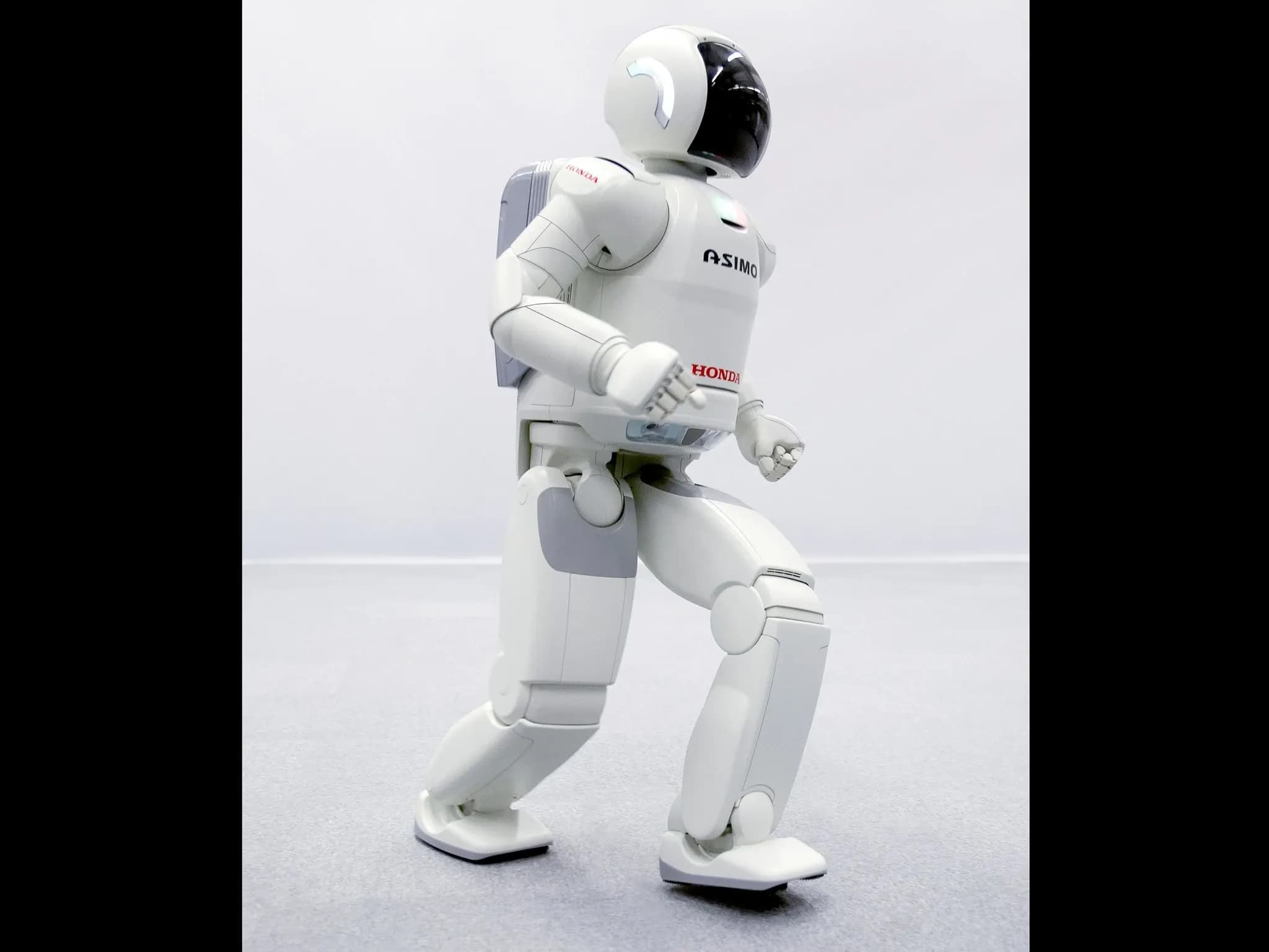 Двуногий белый робот ASIMO делает шаг.