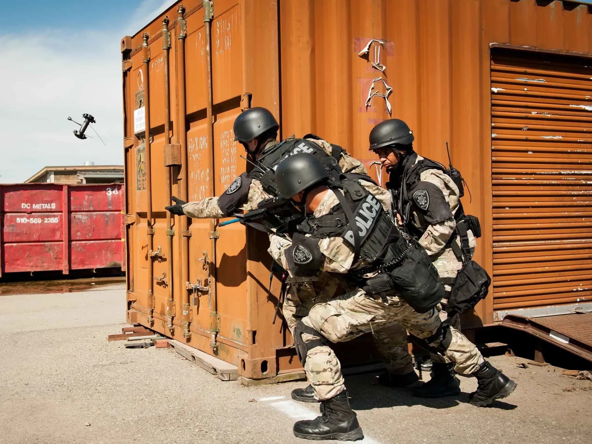 Трое бойцов SWAT в снаряжении и камуфляже укрываются за стеной, один бросает Throwbot.
