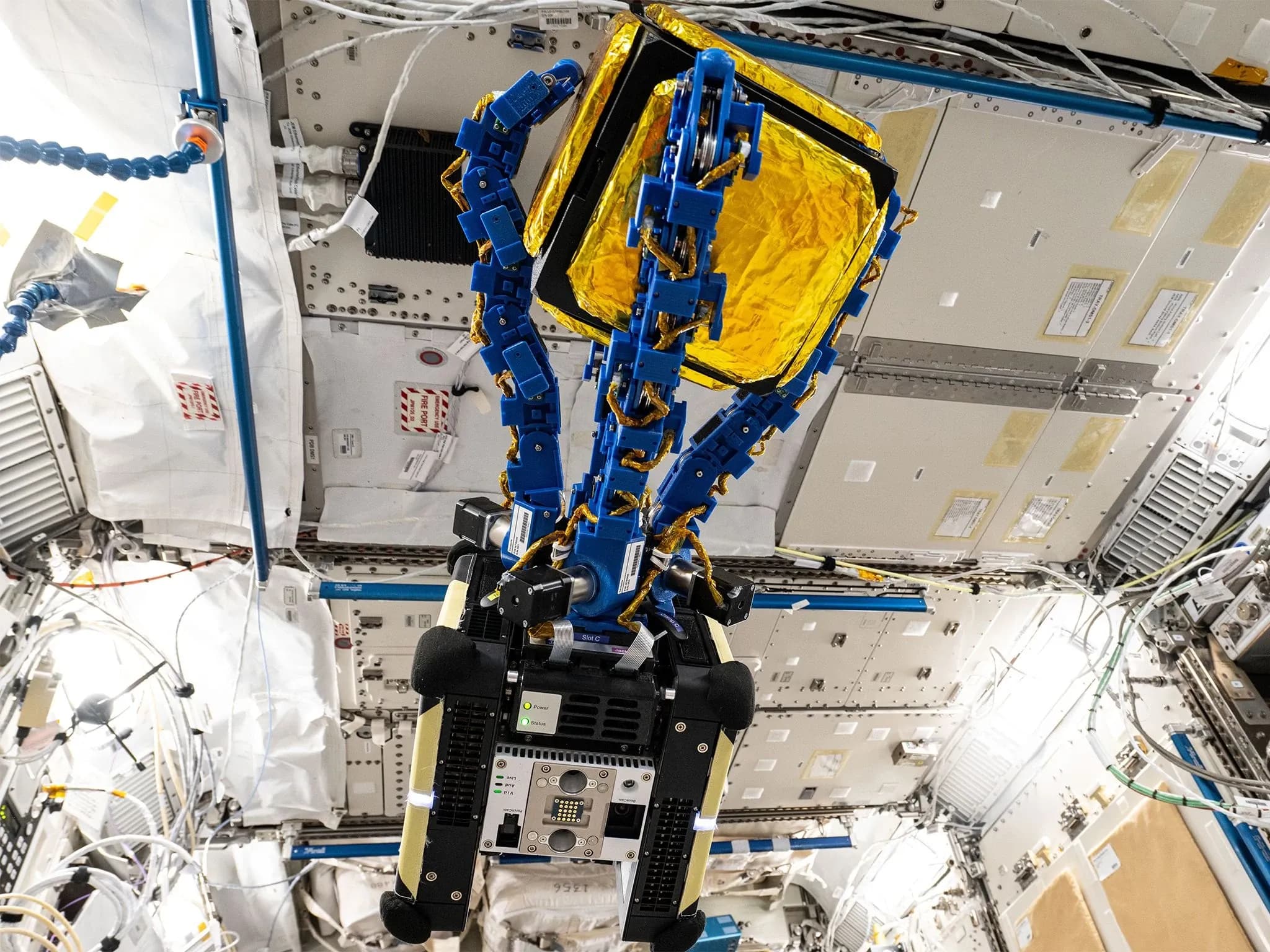 Astrobee — парящий космический робот размером с тостер с четырьмя синими захватами, удерживающими золотой куб, на борту Международной космической станции.