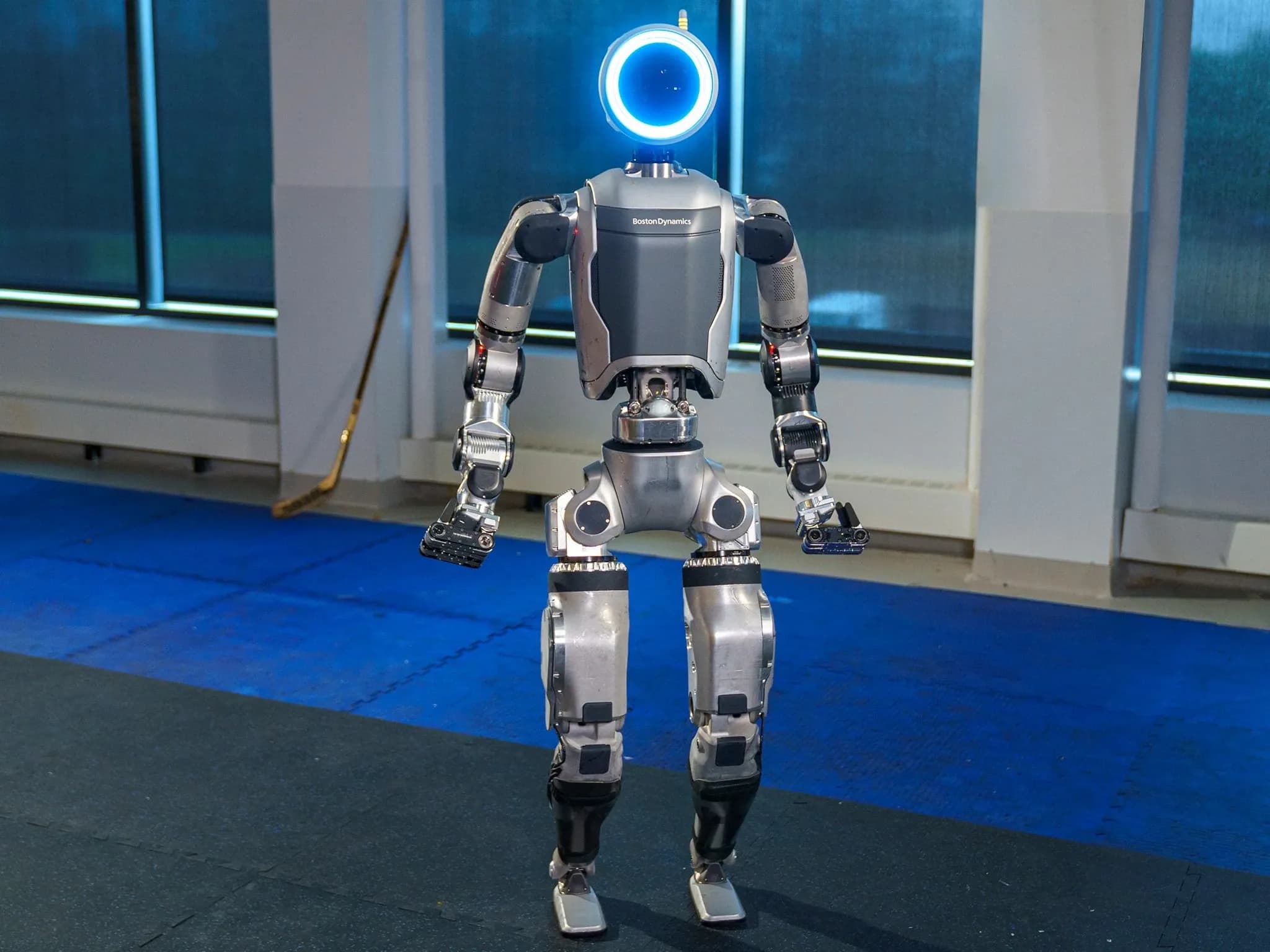 Atlas от Boston Dynamics — двуногий робот серебристо-серого цвета с круглой головой, светящейся синим, длинными руками и захватными кистями.