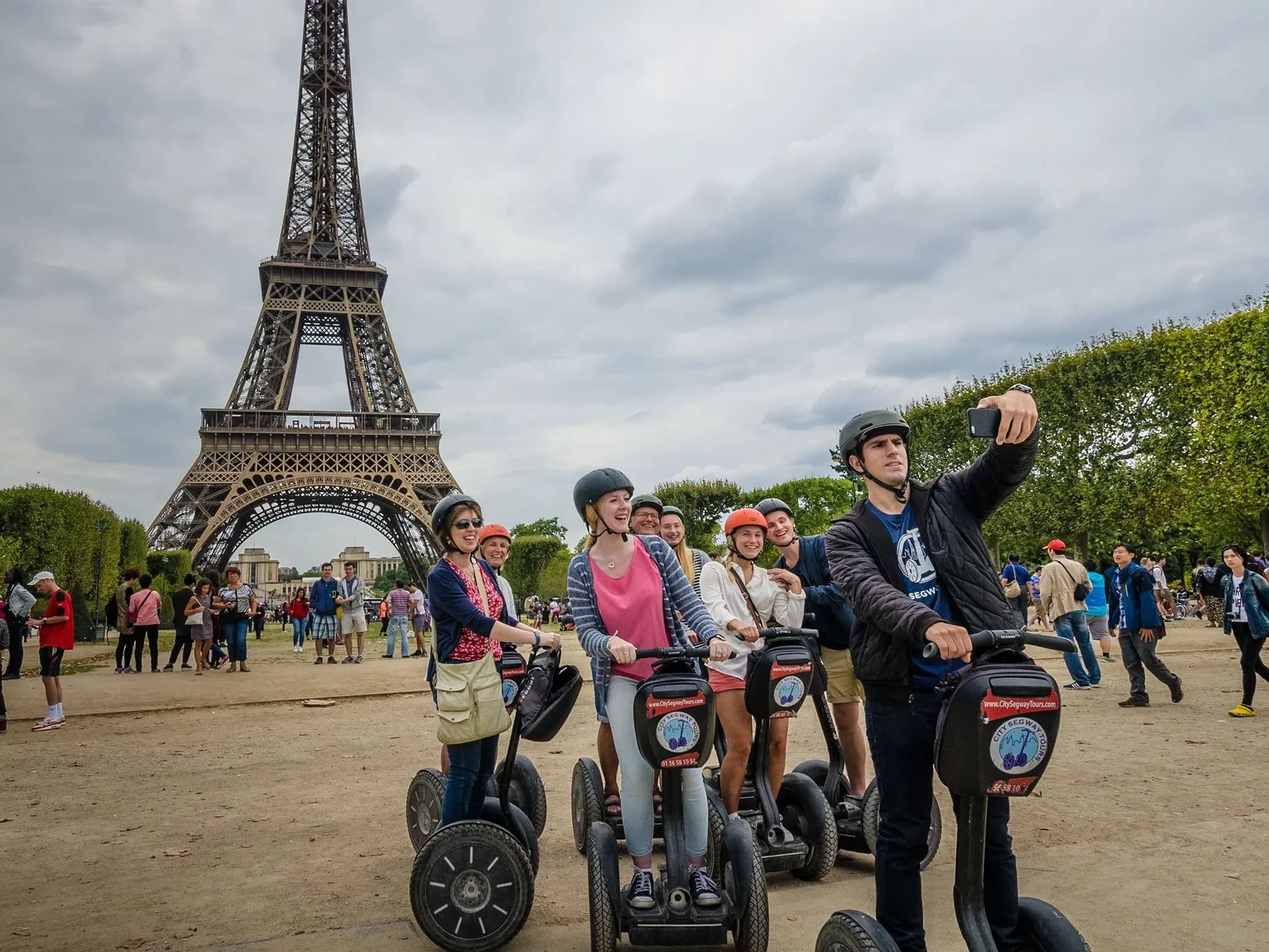 Человек на Segway делает селфи с группой других райдеров на Segway на фоне Эйфелевой башни.
