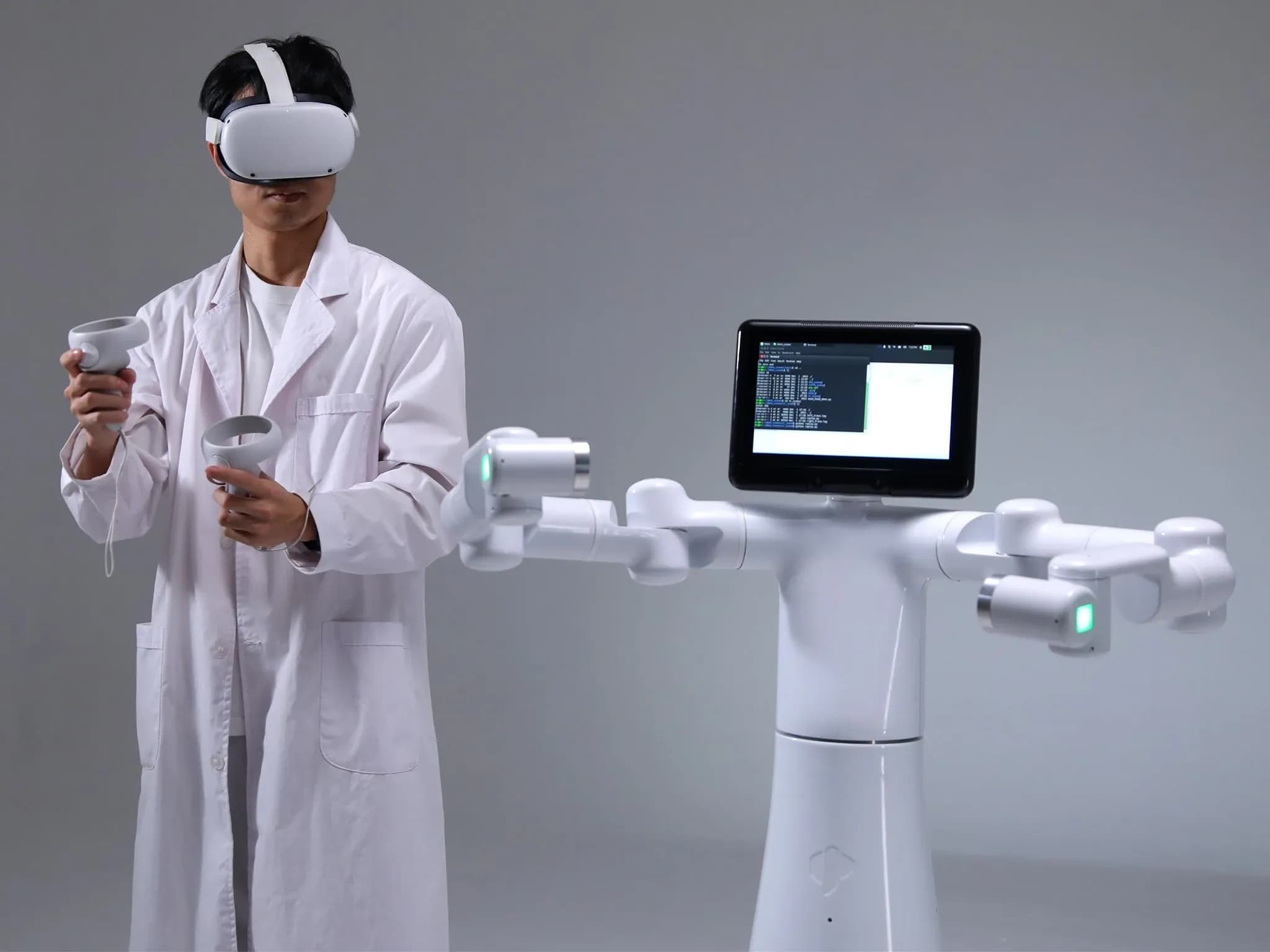 Человек в лабораторном халате и VR-шлеме стоит рядом с колёсным роботом-гуманоидом, у которого вместо головы — планшет.